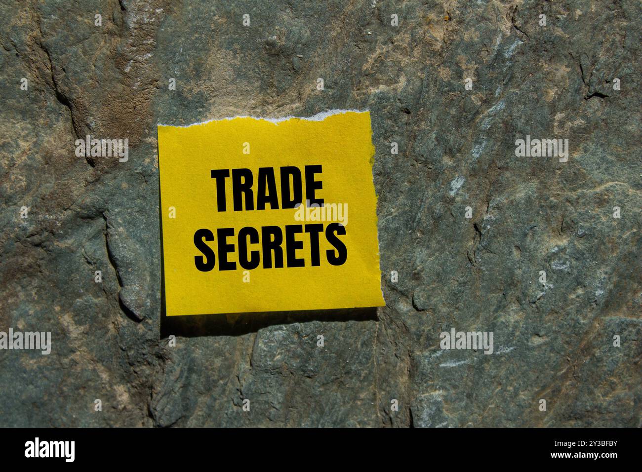 Messaggio segreto commerciale scritto su un pezzo di carta strappato giallo con sfondo in pietra. Simbolo dei segreti commerciali concettuali. Copia spazio. Foto Stock