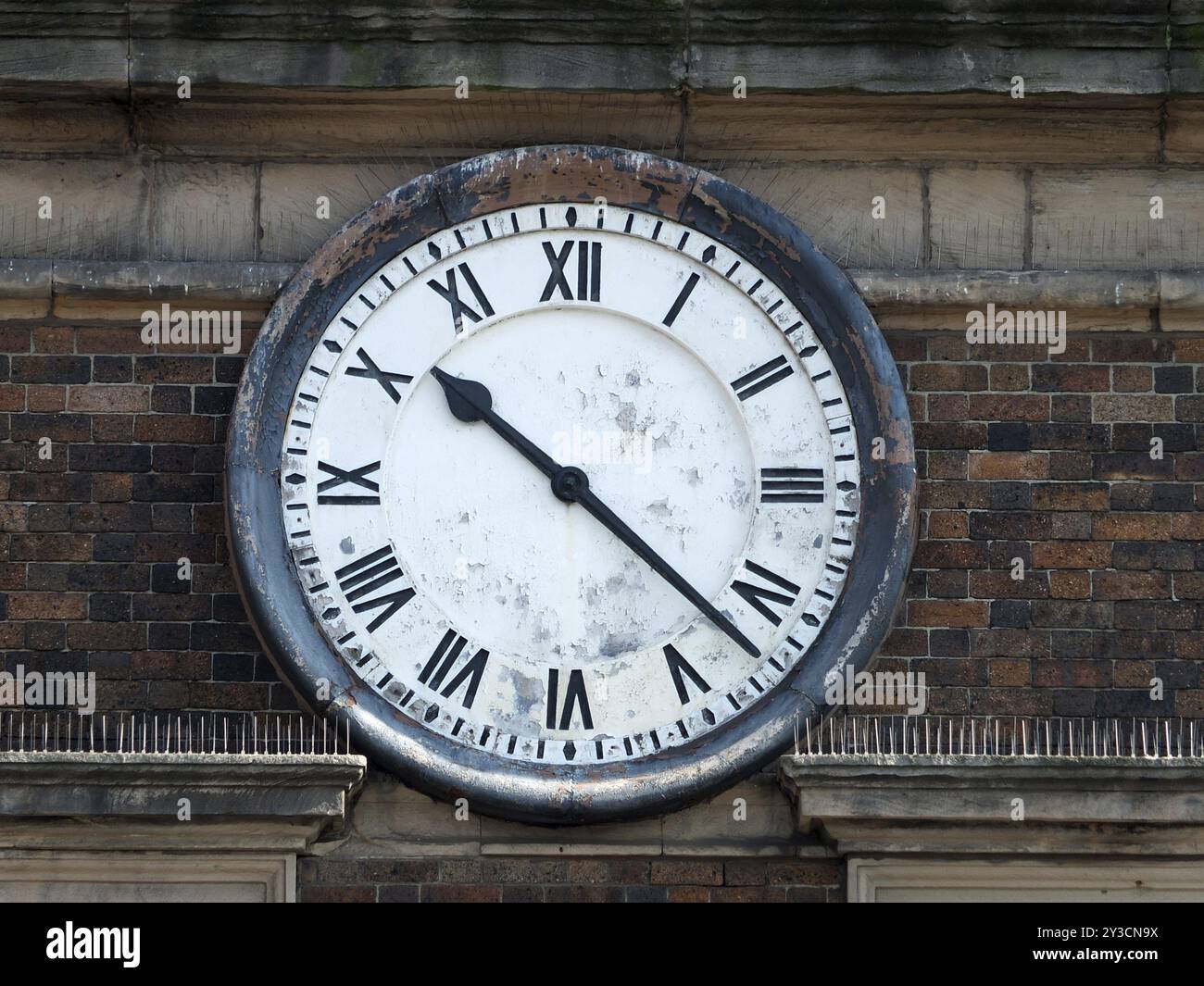 Vecchio orologio aperto 24 ore su 24 sulle pareti di mattoni di un edificio con numeri romani e volto sbucciato con le mani alle dieci e venti Foto Stock