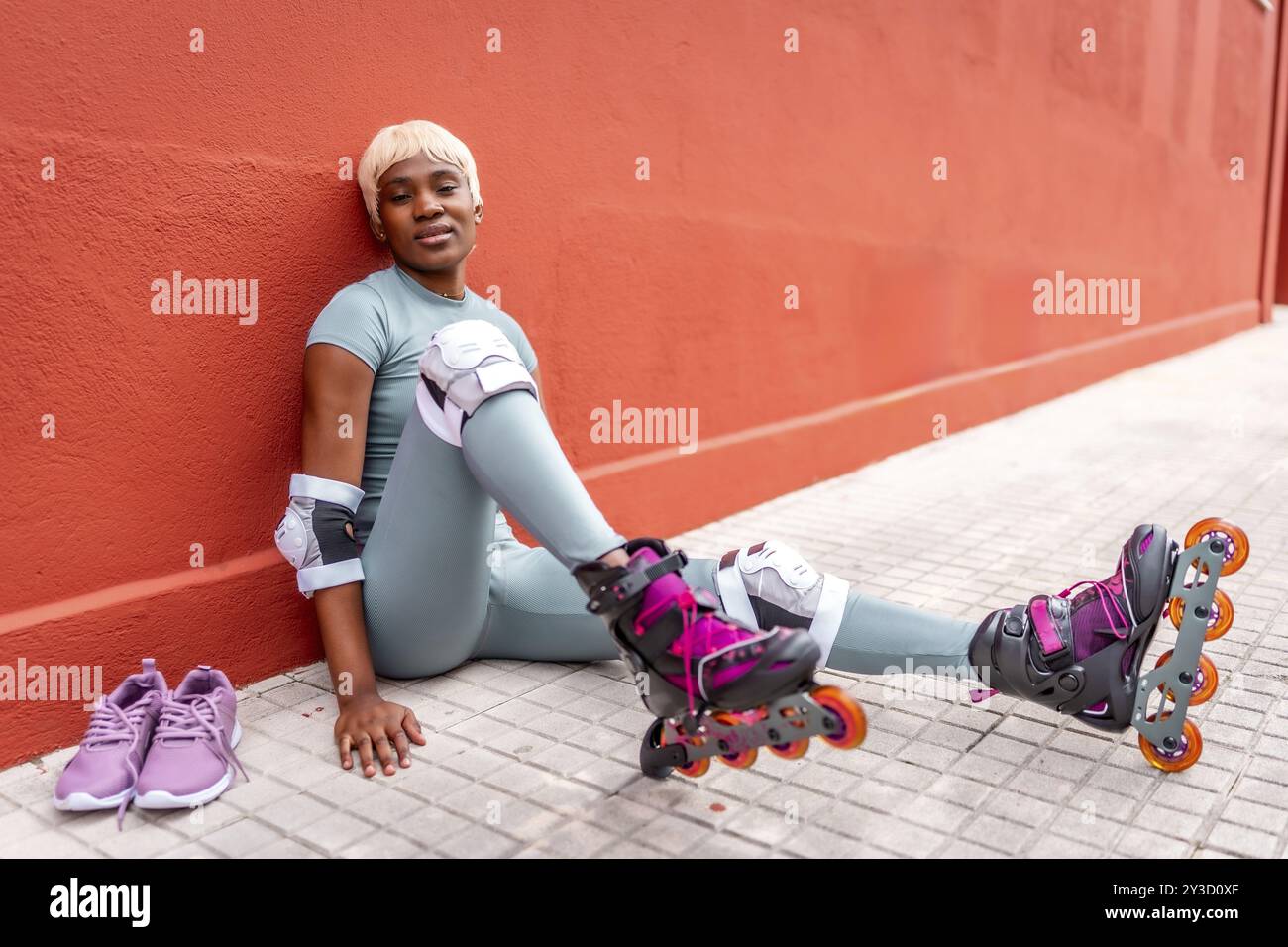 Donna urbana africana seduta per terra in strada con pattini in linea Foto Stock