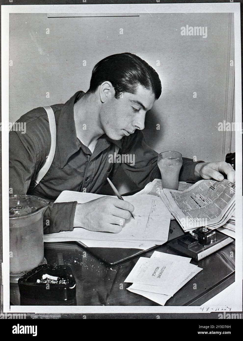 Joe DiMaggio, esterno dei New York Yankees della American League, ha un bicchiere di tè ghiacciato accanto a lui mentre controlla le colonne di home run nelle pagine sportive quotidiane, New York, New York, 1949. Foto della United States Information Agency Foto Stock