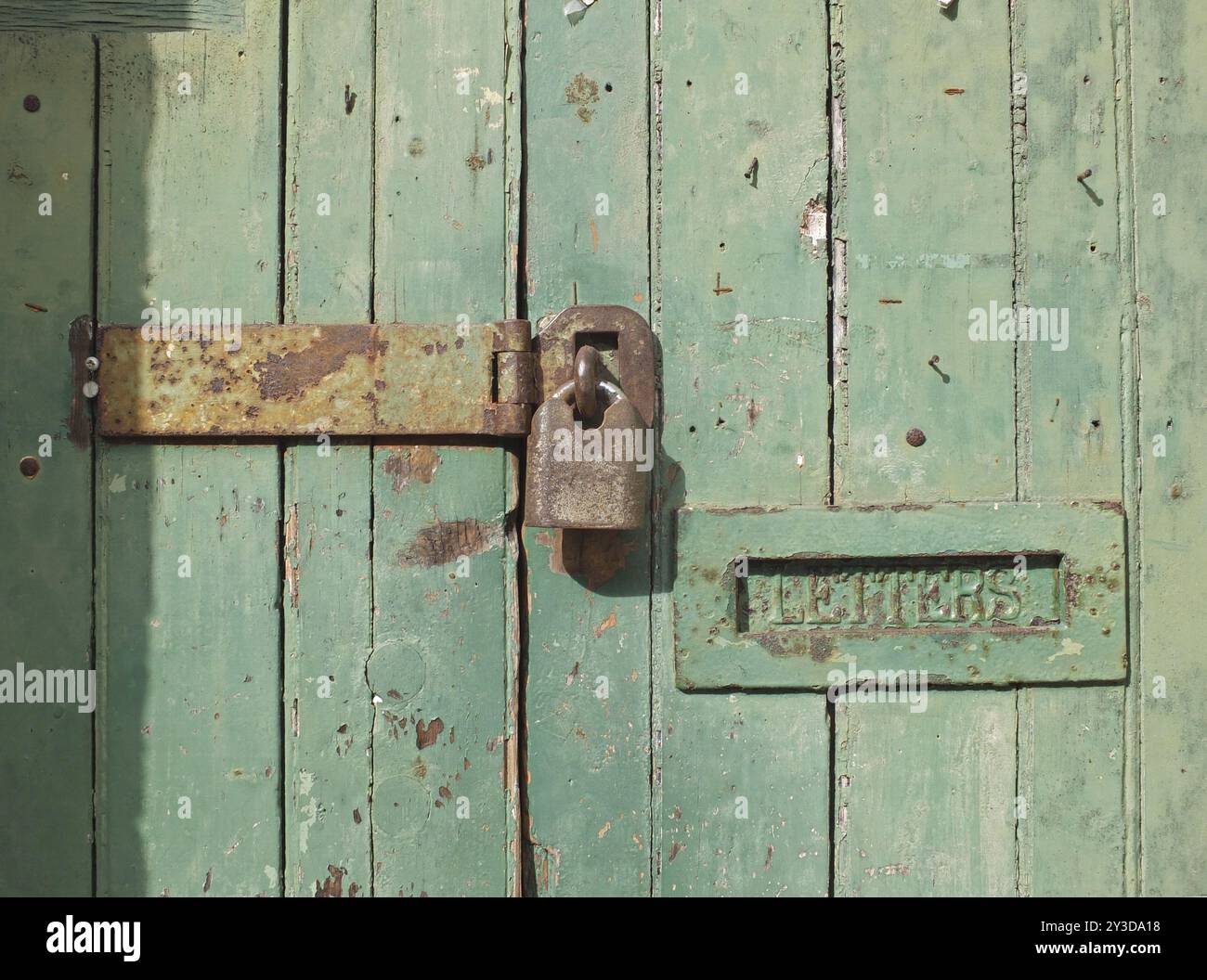 Primo piano di una vecchia porta di legno con vernice verde sbiadita, un lucchetto chiuso arrugginito e una vecchia cassetta delle lettere in metallo Foto Stock