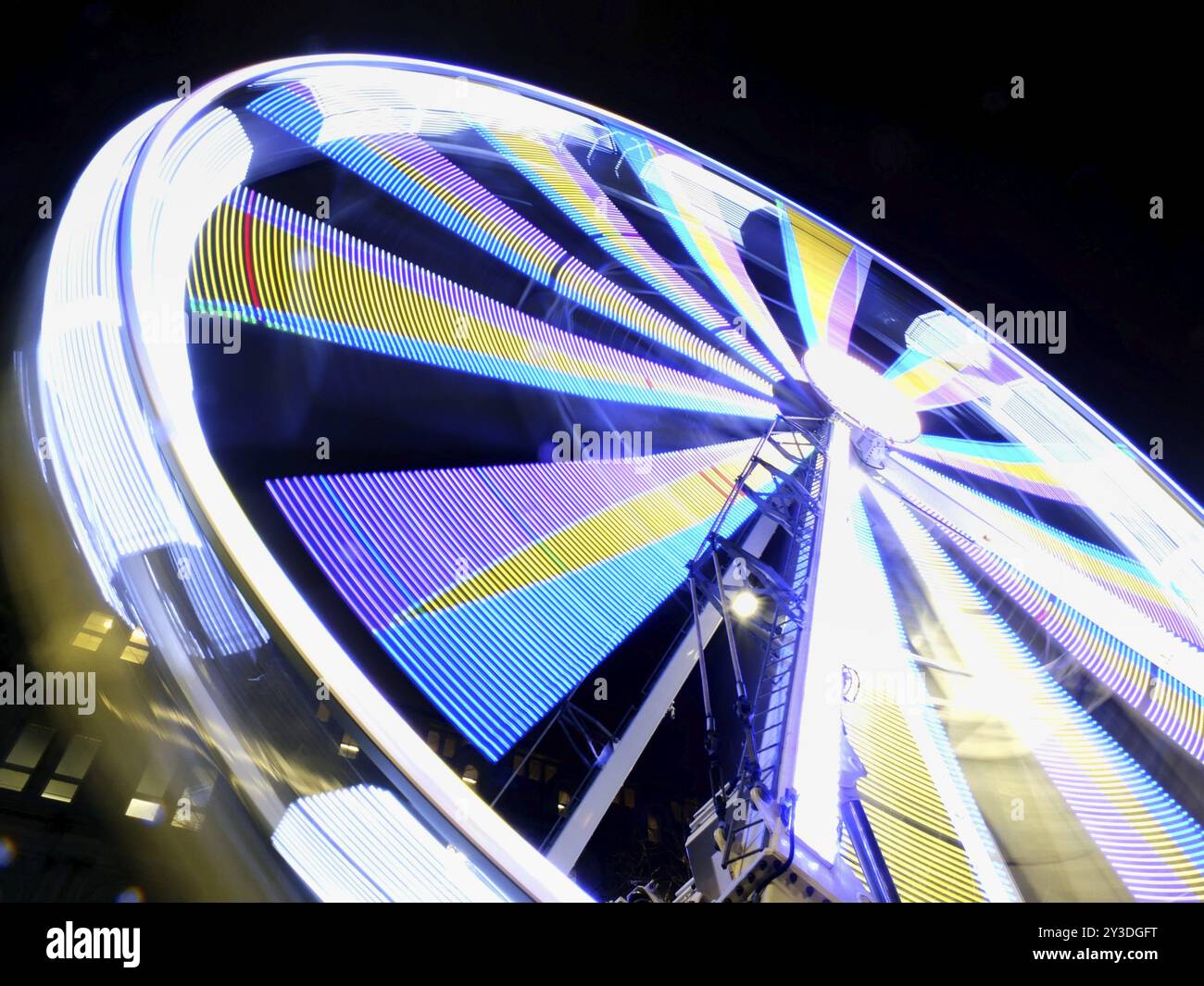 Una sfocatura notturna con movimento a lunga esposizione di una ruota panoramica rotante illuminata con colori al neon brillanti Foto Stock