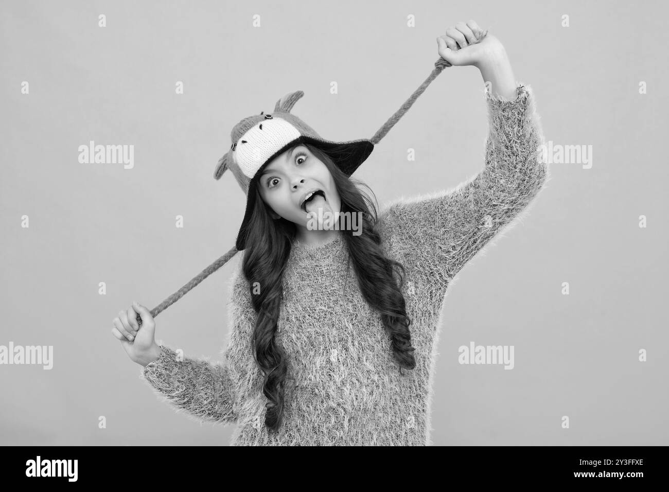 Moderna ragazza adolescente che indossa un maglione e un cappello a maglia su sfondo giallo isolato. Faccia divertente Foto Stock