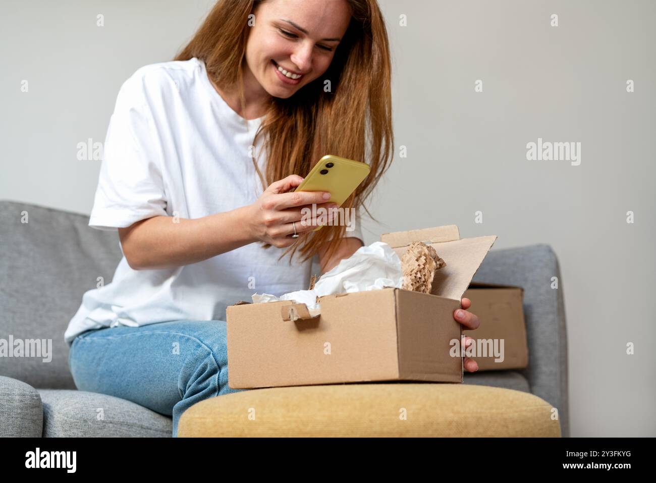 Donna che condivide le foto del suo ordine online dal suo cellulare. Disimballaggio dell'acquisto online e della fotografia di prodotti o invio di feedback al venditore. E-c Foto Stock