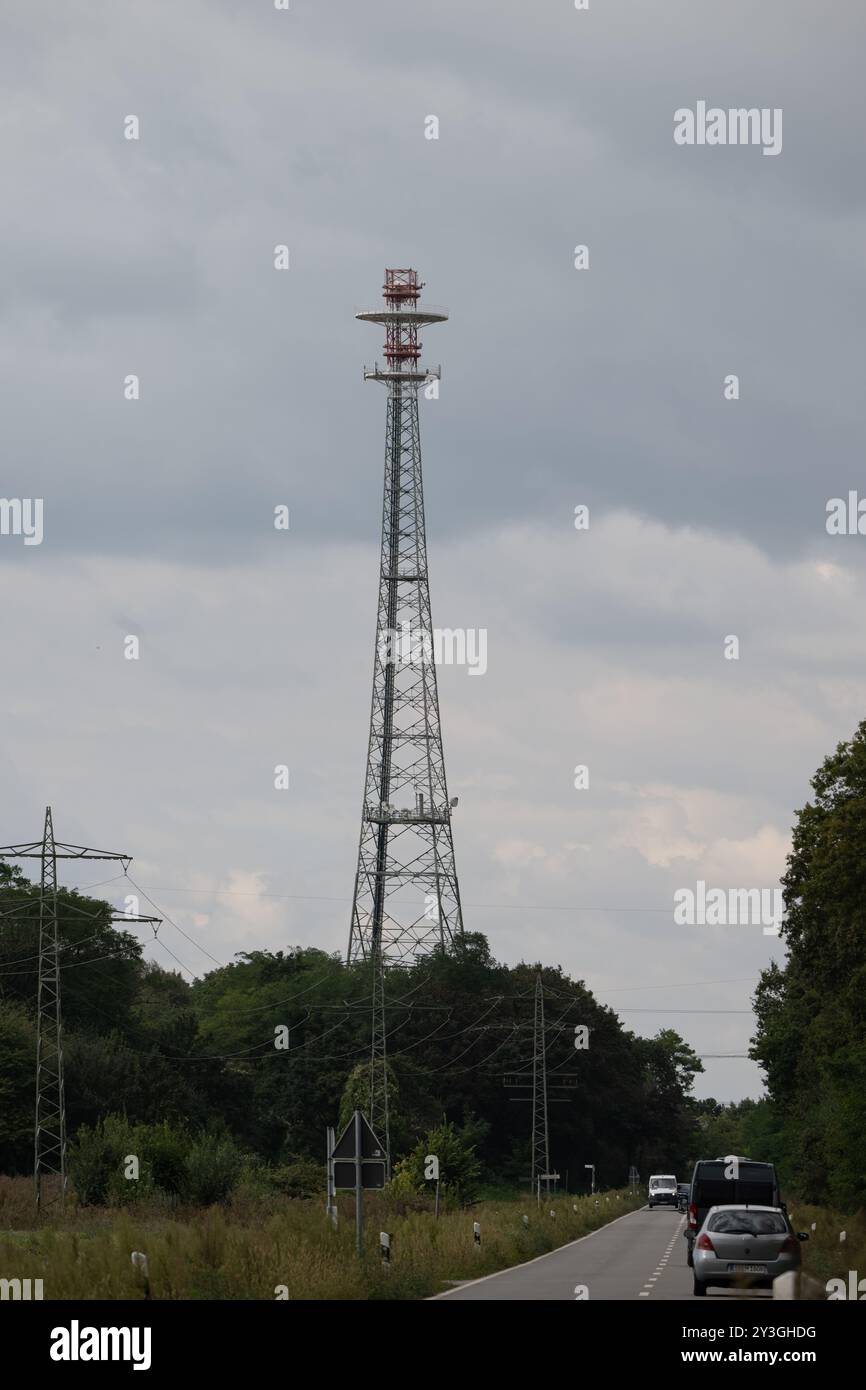 Deutschland, Rheinland-Pfalz, Mutterstadt, 13.09.2024. Ein hoher Richtfunkmast steht neben einer ruhigen Landstrasse, umgeben von Baeumen, unter einem Foto Stock