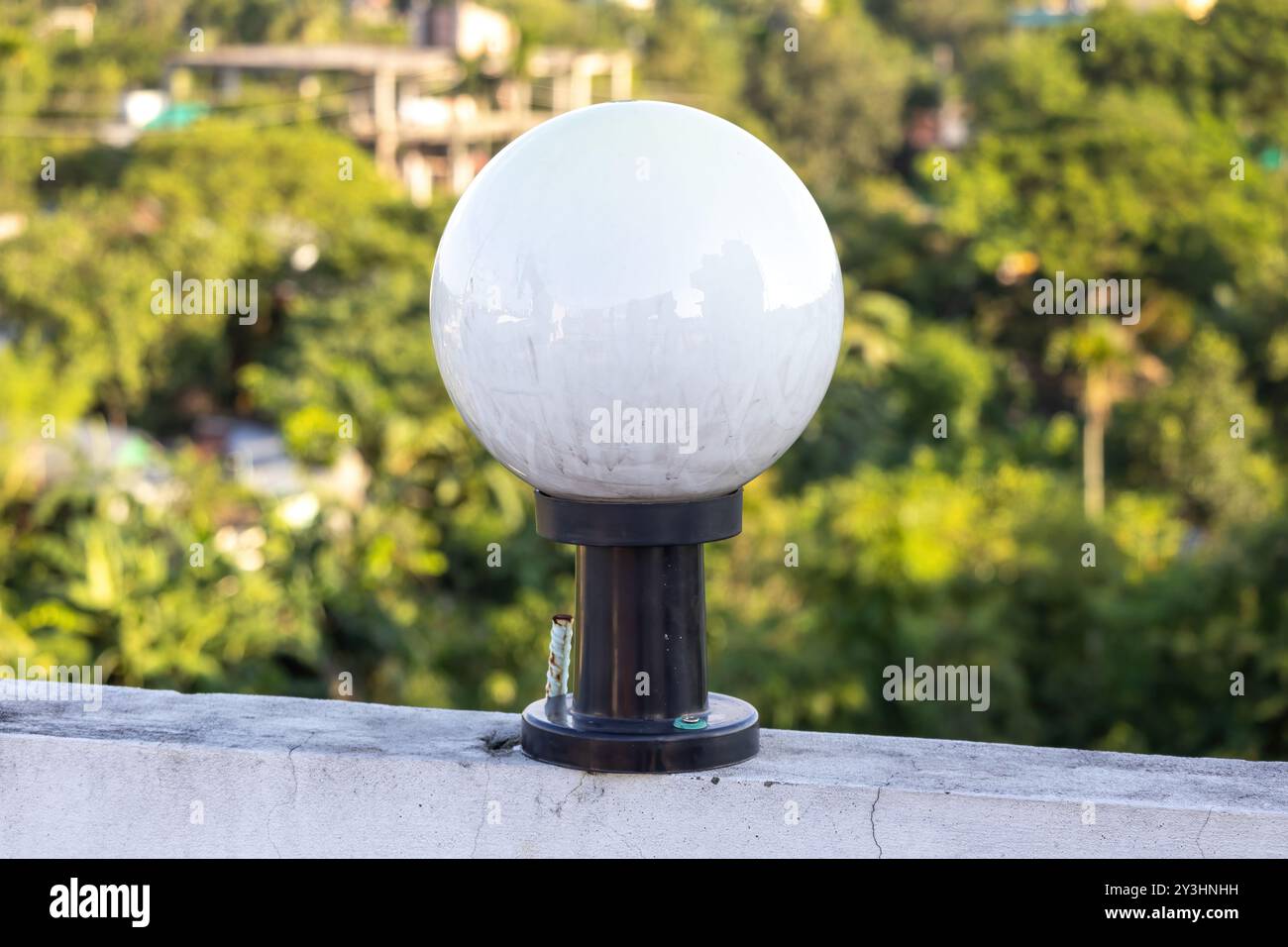 Lampada rotonda bianca in vetro su asta in acciaio nero montata sulla parete della casa, sfondo naturale sfocato. Foto Stock