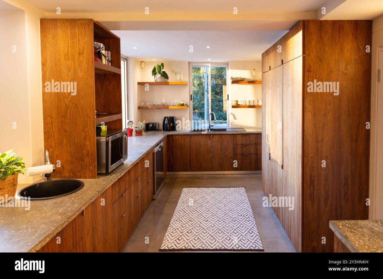 A casa, la luce del sole scorre attraverso la finestra in una cucina moderna con armadi ed elettrodomestici in legno Foto Stock