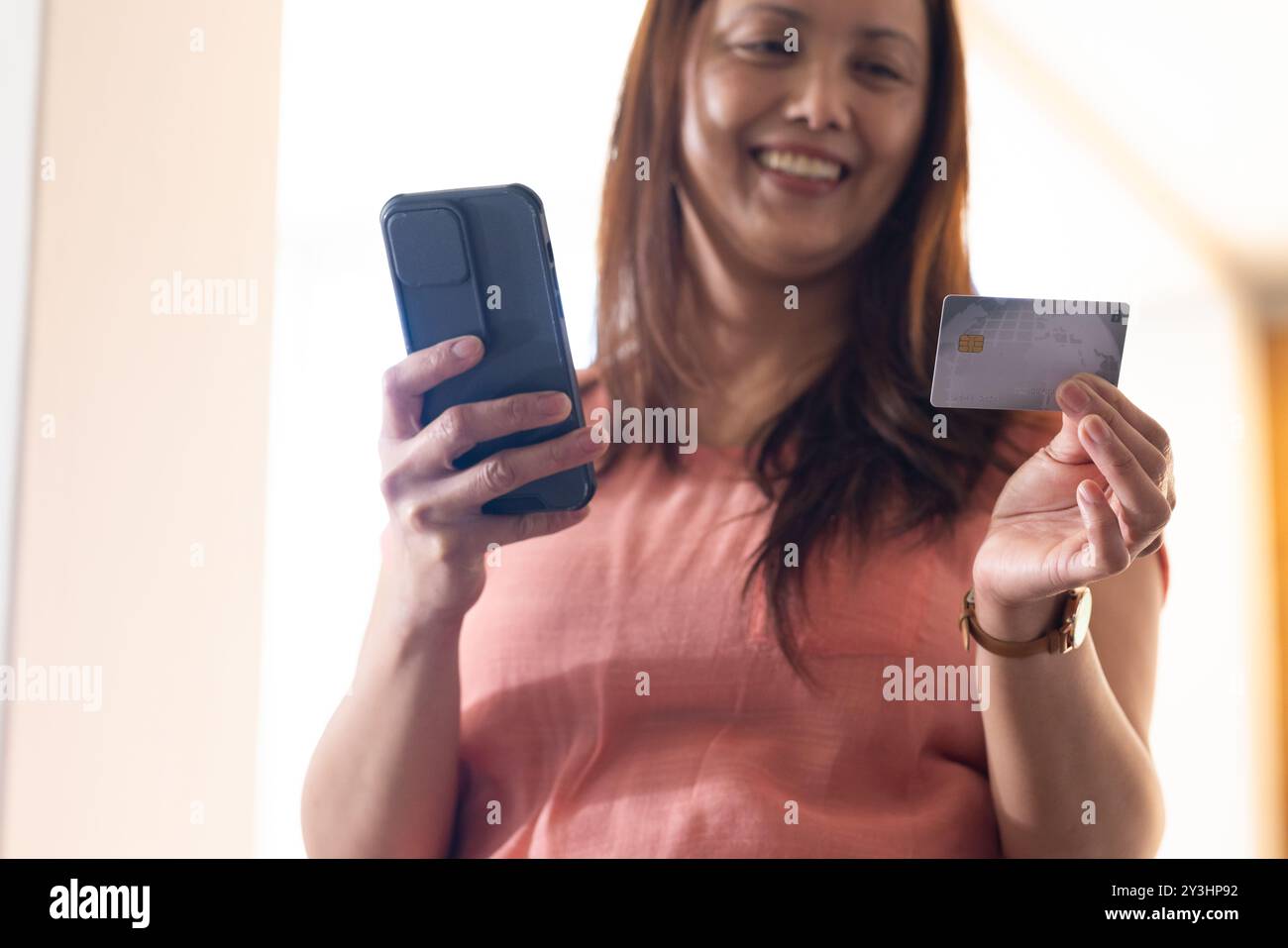 A casa, con smartphone e carta di credito, donna asiatica sorridente e che effettua pagamenti online Foto Stock