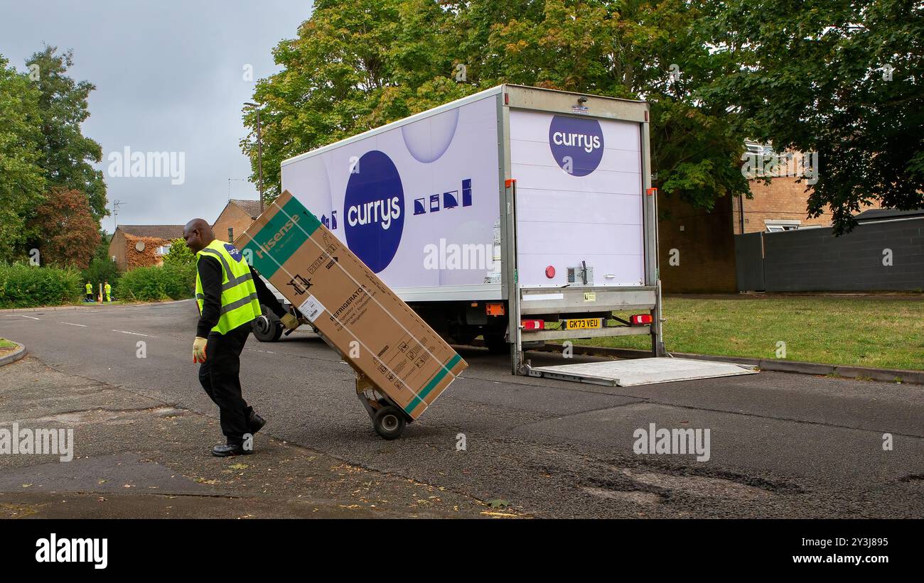 Milton Keynes, Regno Unito - 3 settembre 2024: Il corriere Currys, in un giubbotto ad alta visibilità, consegna un nuovo frigorifero, in una scatola di cartone, su un carrello in una casa britannica Foto Stock