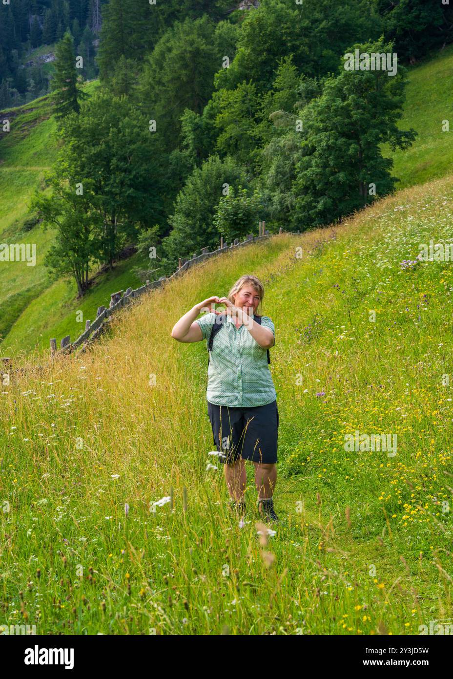 Una donna allegramente sorridente di mezza età ama un viaggio in montagna. Ha creato un cuore con le mani. Escursioni, avventure e vita di mezza età. Foto Stock