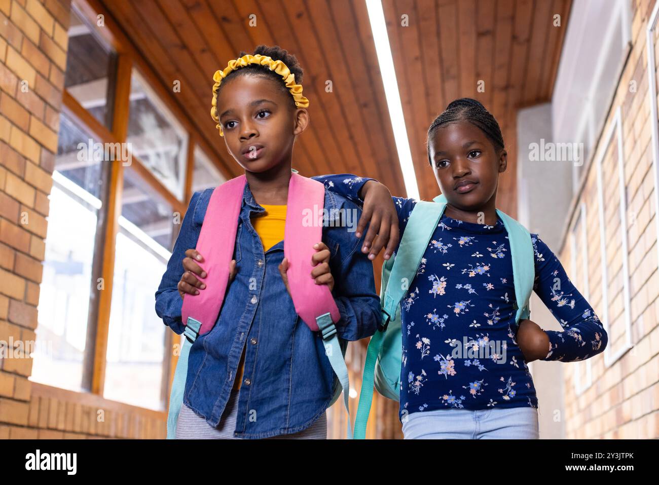 Camminando nel corridoio della scuola, due ragazze afroamericane con zaini che guardano avanti Foto Stock