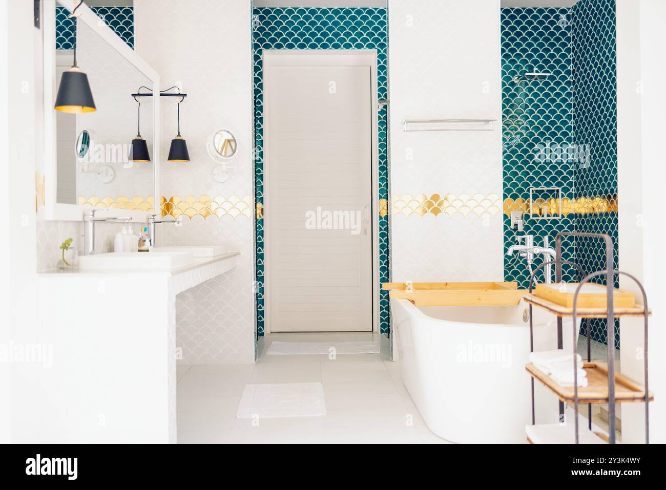 Un bagno elegante presenta un mix di piastrelle blu e bianche a base di pesce. Un grande specchio e moderne luci a sospensione nere sono appese sopra i lavandini. L'oro AC Foto Stock