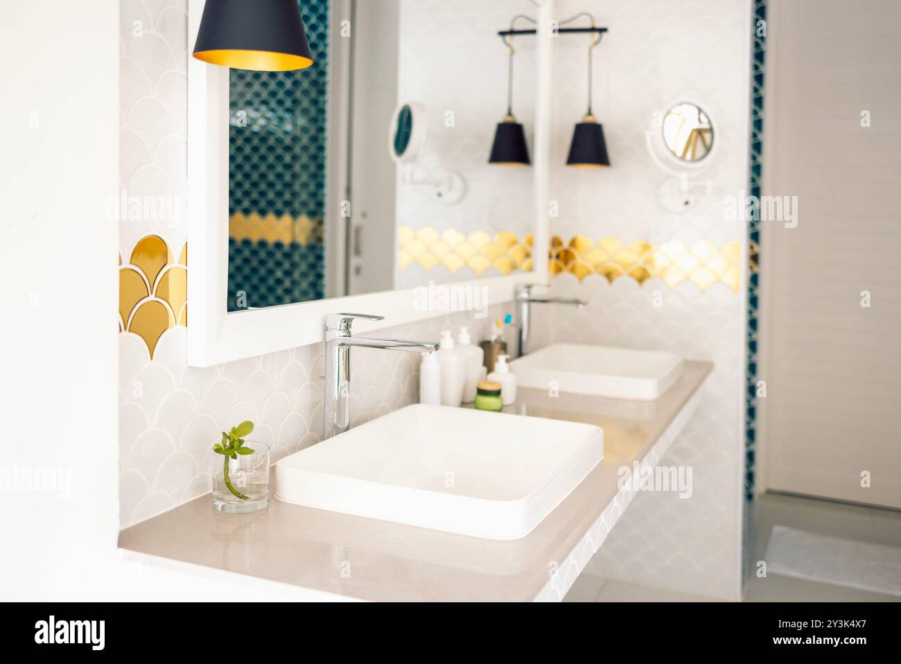 Un bagno elegante presenta un mix di piastrelle blu e bianche a base di pesce. Un grande specchio e moderne luci a sospensione nere sono appese sopra i lavandini. L'oro AC Foto Stock