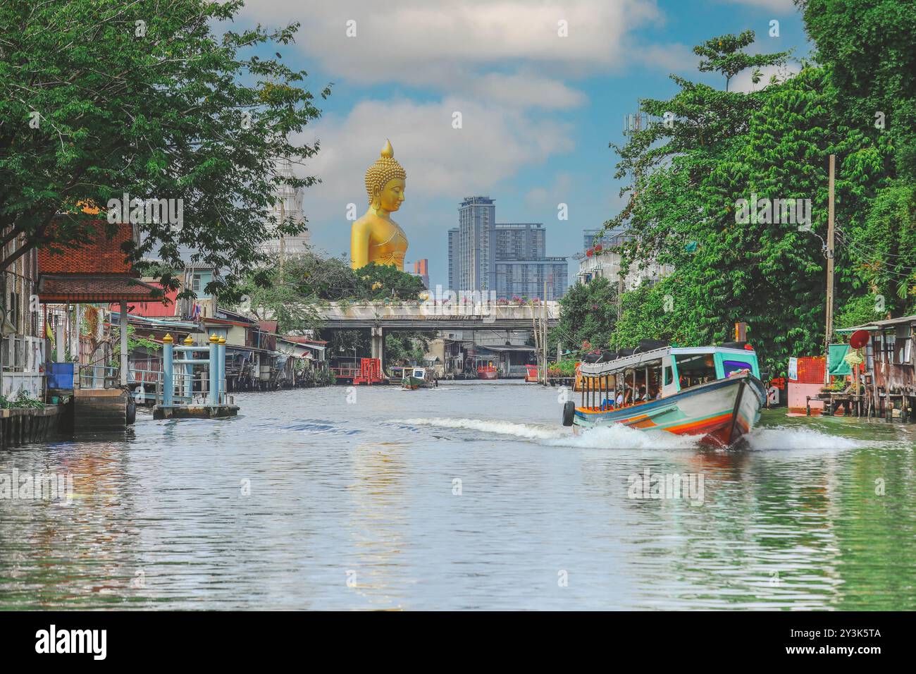 Vista della grande statua del Buddha a Bangkok, Thailandia (Wat Pak Nam Phasi Charoen) dal canale con case di legno e barche a coda lunga Foto Stock