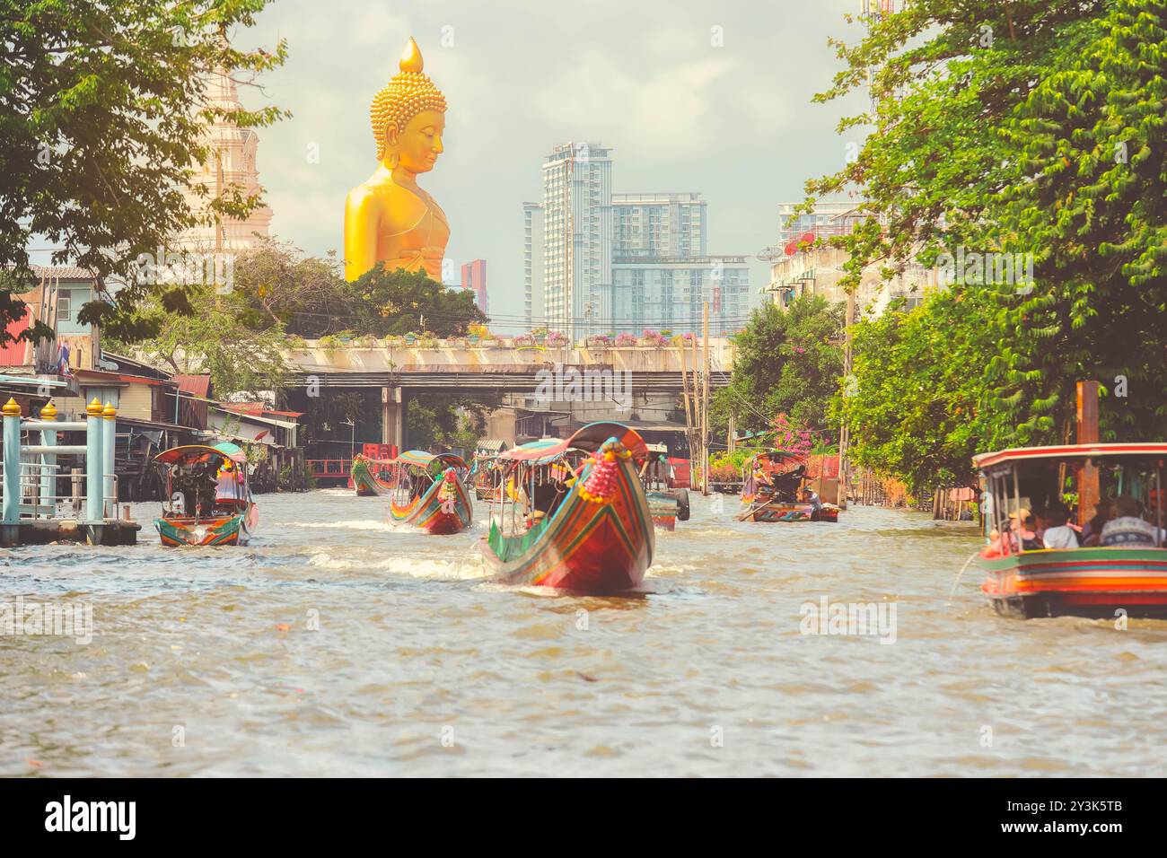 Vista della grande statua del Buddha a Bangkok, Thailandia (Wat Pak Nam Phasi Charoen) dal canale con case di legno e barche a coda lunga Foto Stock