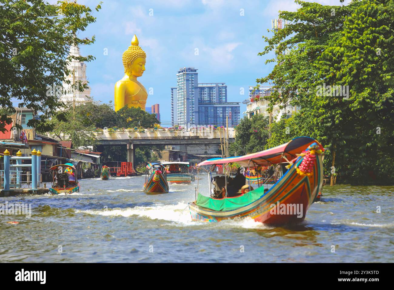 Vista della grande statua del Buddha a Bangkok, Thailandia (Wat Pak Nam Phasi Charoen) dal canale con case di legno e barche a coda lunga Foto Stock