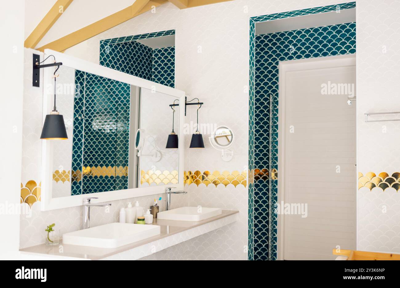 Un bagno elegante presenta un mix di piastrelle blu e bianche a base di pesce. Un grande specchio e moderne luci a sospensione nere sono appese sopra i lavandini. L'oro AC Foto Stock