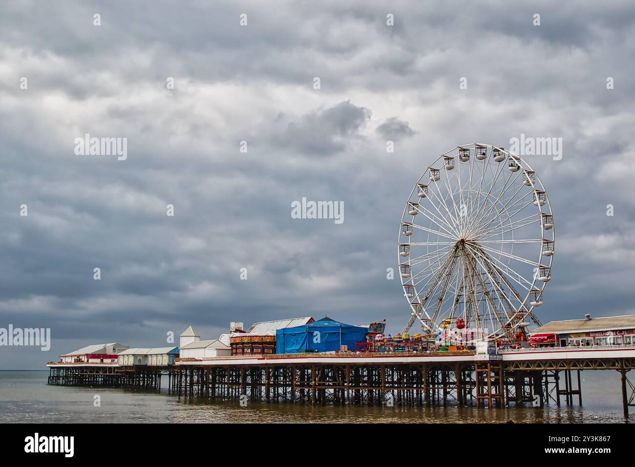 Una vista panoramica di un molo con una grande ruota panoramica, con cieli nuvolosi in alto. Il molo è fiancheggiato da edifici colorati e attrazioni, riflettono Foto Stock