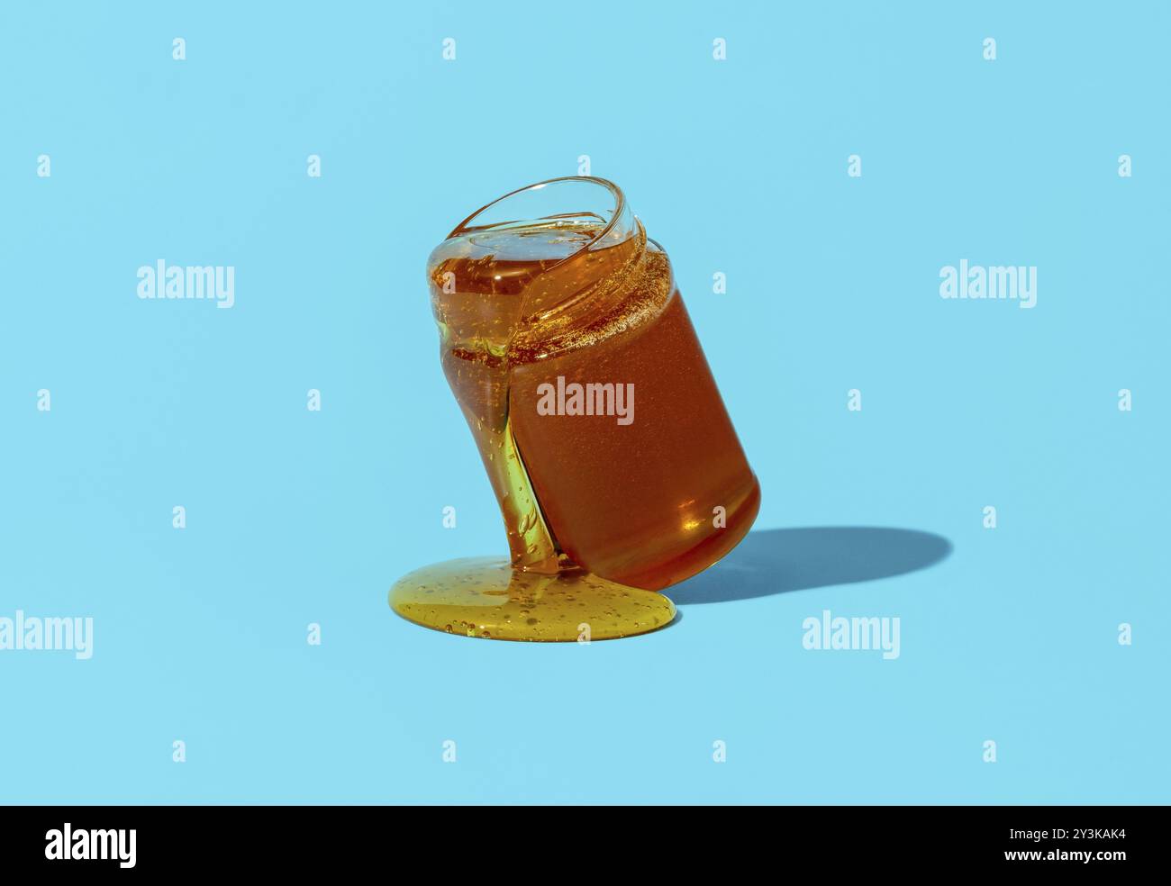 Barattolo con miele minimalista su un tavolo blu. Gocciolamento di miele da un vaso di vetro direttamente sul tavolo Foto Stock