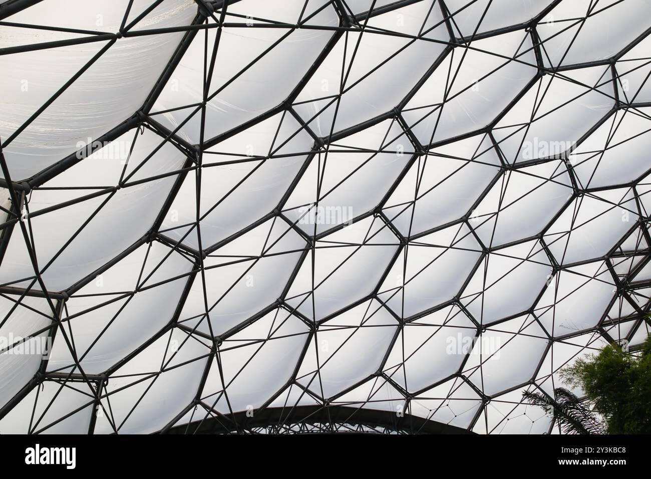 Vista ravvicinata di una moderna struttura architettonica caratterizzata da un tetto geometrico e traslucido sostenuto da una struttura metallica. Il design presenta un ser Foto Stock