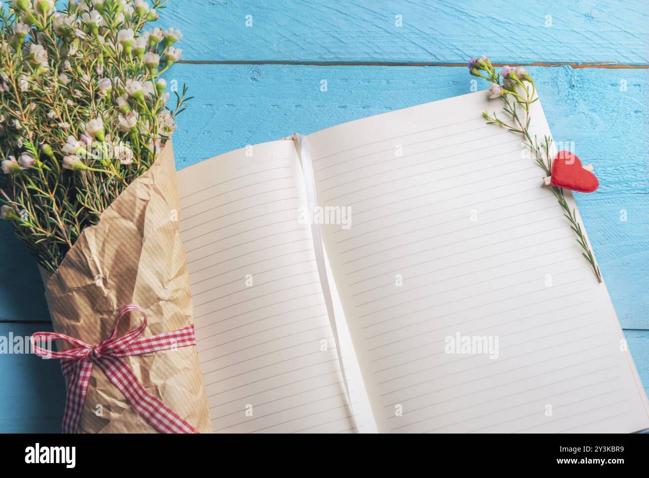 Apri pagine di quaderni con un piccolo bouquet di fiori bianchi e clip di legno a forma di cuore, su sfondo blu. Contesto per la pianificazione di matrimoni. La cornice del giorno delle donne Foto Stock