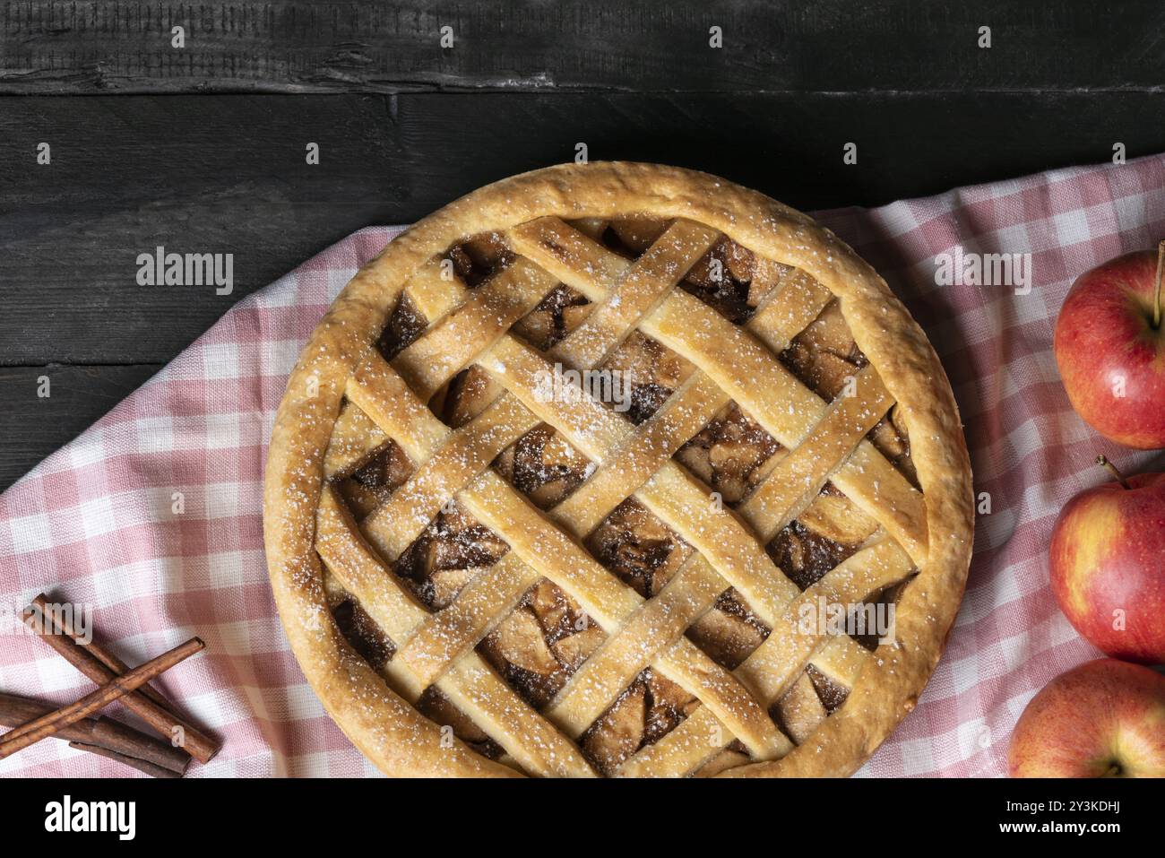 Tavolo rustico con un'intera torta di mele classica su un asciugamano da cucina rosa, circondato da frutta di mele e cannella. Sopra la vista. Dessert fatti in casa Foto Stock