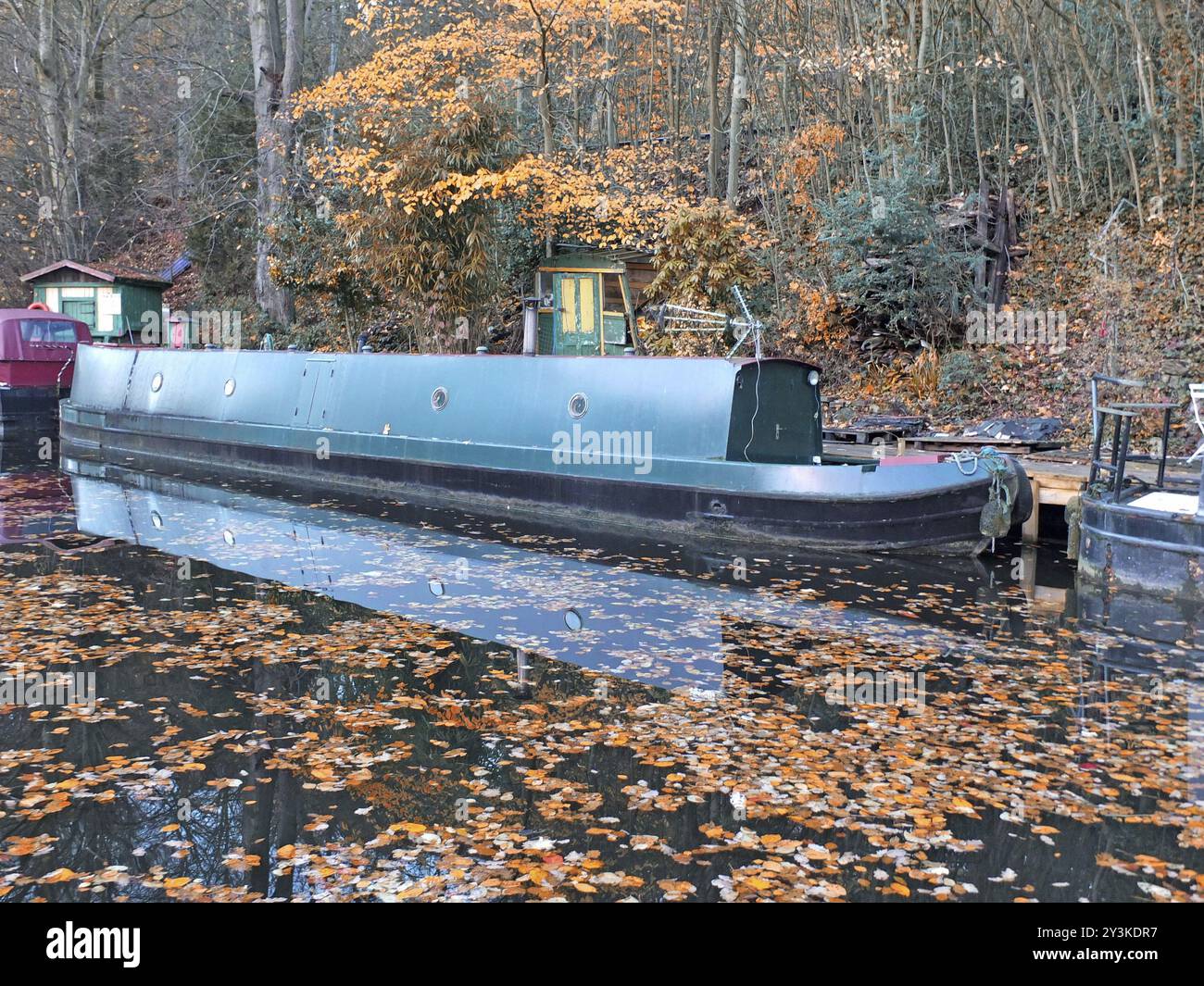 Una vista panoramica di barche strette in un canale circondato da foglie d'autunno dorate con riflessi sull'acqua e sugli alberi della foresta nel ponte di hebden wes Foto Stock