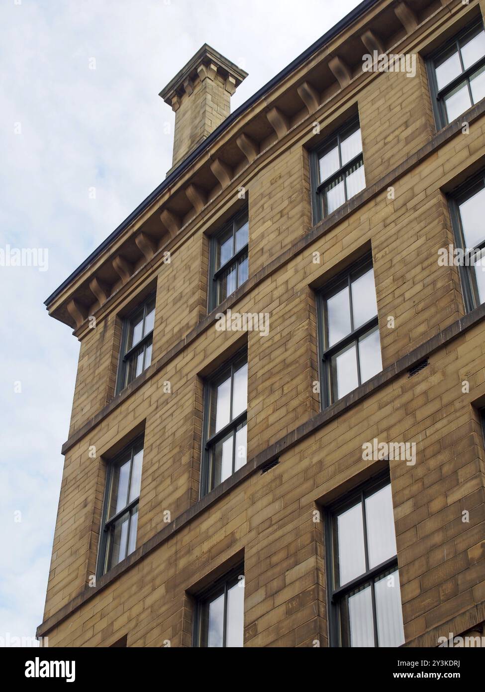 L'angolo di un alto edificio commerciale in pietra del XIX secolo nell'area di Little germany di bradford West yorkshire con camino contro un cielo blu con Foto Stock