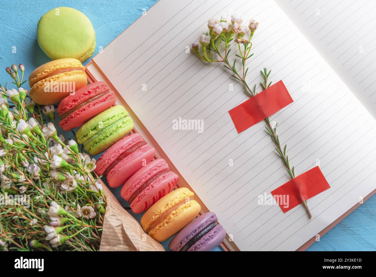 Aprire il notebook con fiore bloccato su di esso, multicolore amaretti e minuscoli fiori bianchi bouquet. Al di sopra di vista del francese dessert e fiori di primavera. Donne d Foto Stock