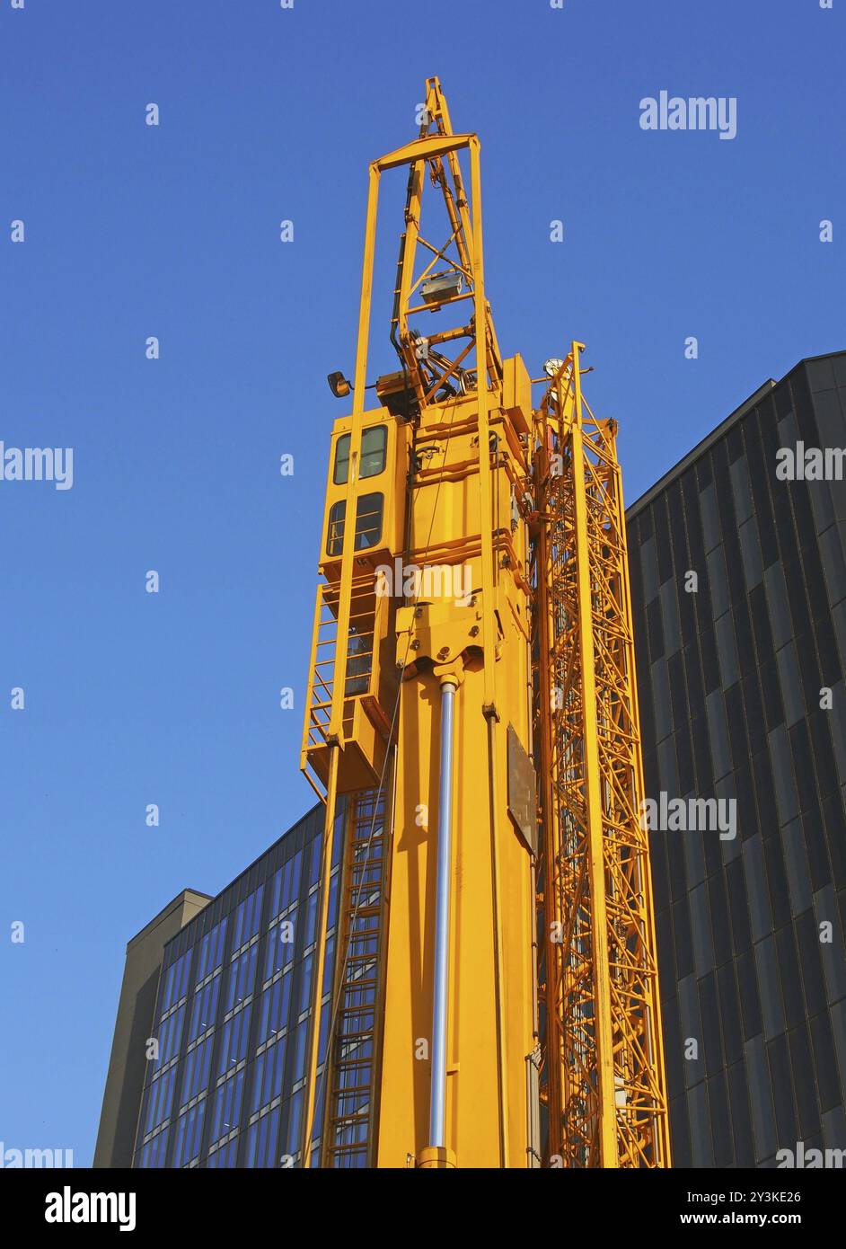 Una gru da cantiere gialla ripiegata con cavalletto fissato lateralmente in attesa di essere dispiegato in un cantiere urbano Foto Stock