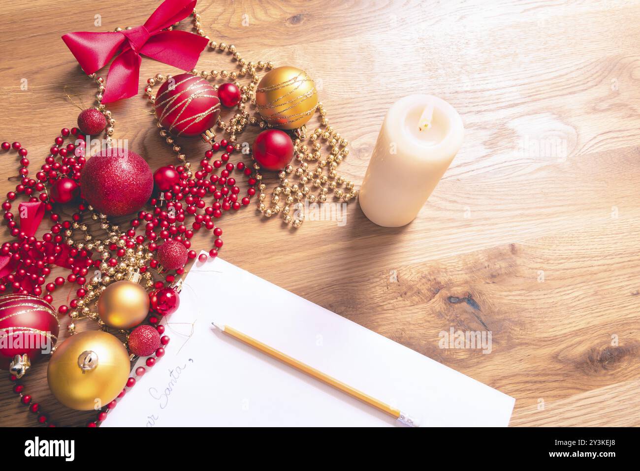 Immagine concettuale con una lettera indirizzata a Babbo Natale, su un tavolo di legno, circondata da decorazioni natalizie e da una candela accesa Foto Stock