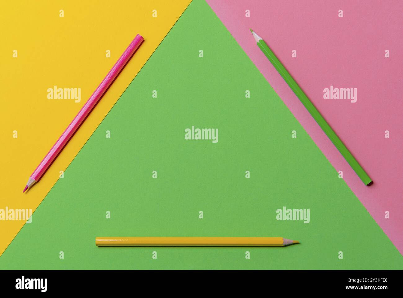Scrivania in tre colori con matite in legno in verde, giallo e rosa, geometrica visualizzata in un triangolo. Sopra la vista con spazio di copia. Torna a scuola Foto Stock