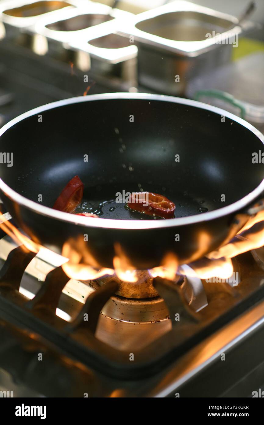 Uno chef cuoce peperoni rossi in una teglia calda usando pinze nella cucina dell'hotel, mostrando l'arte di cucinare con ingredienti freschi Foto Stock