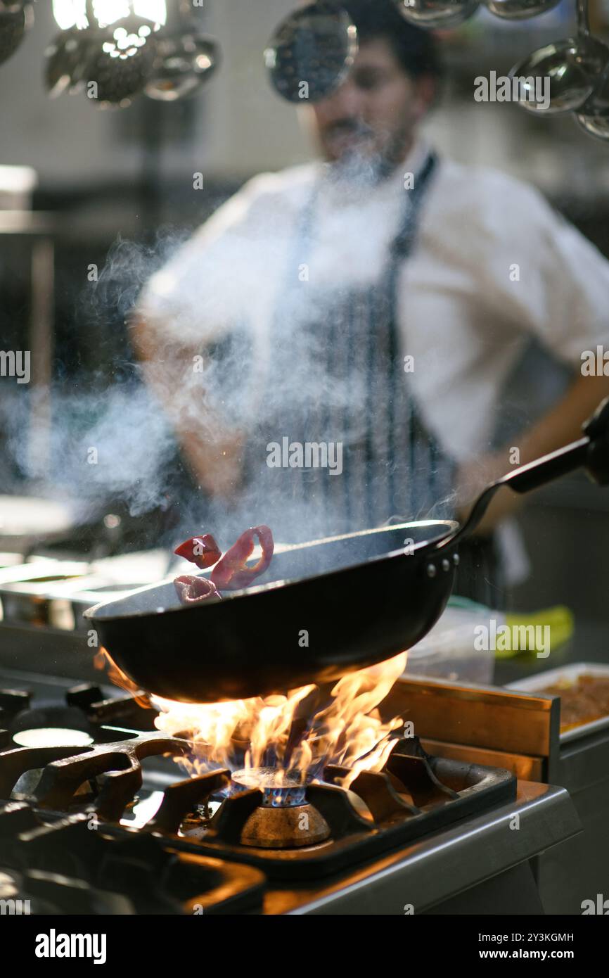 Uno chef cuoce peperoni rossi in una teglia calda usando pinze nella cucina dell'hotel, mostrando l'arte di cucinare con ingredienti freschi Foto Stock