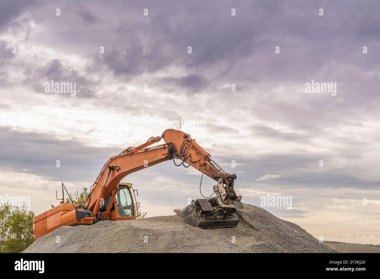 Escavatore arancione pesante con benna grande che lavora sulla parte superiore di un cumulo di zavorre Foto Stock