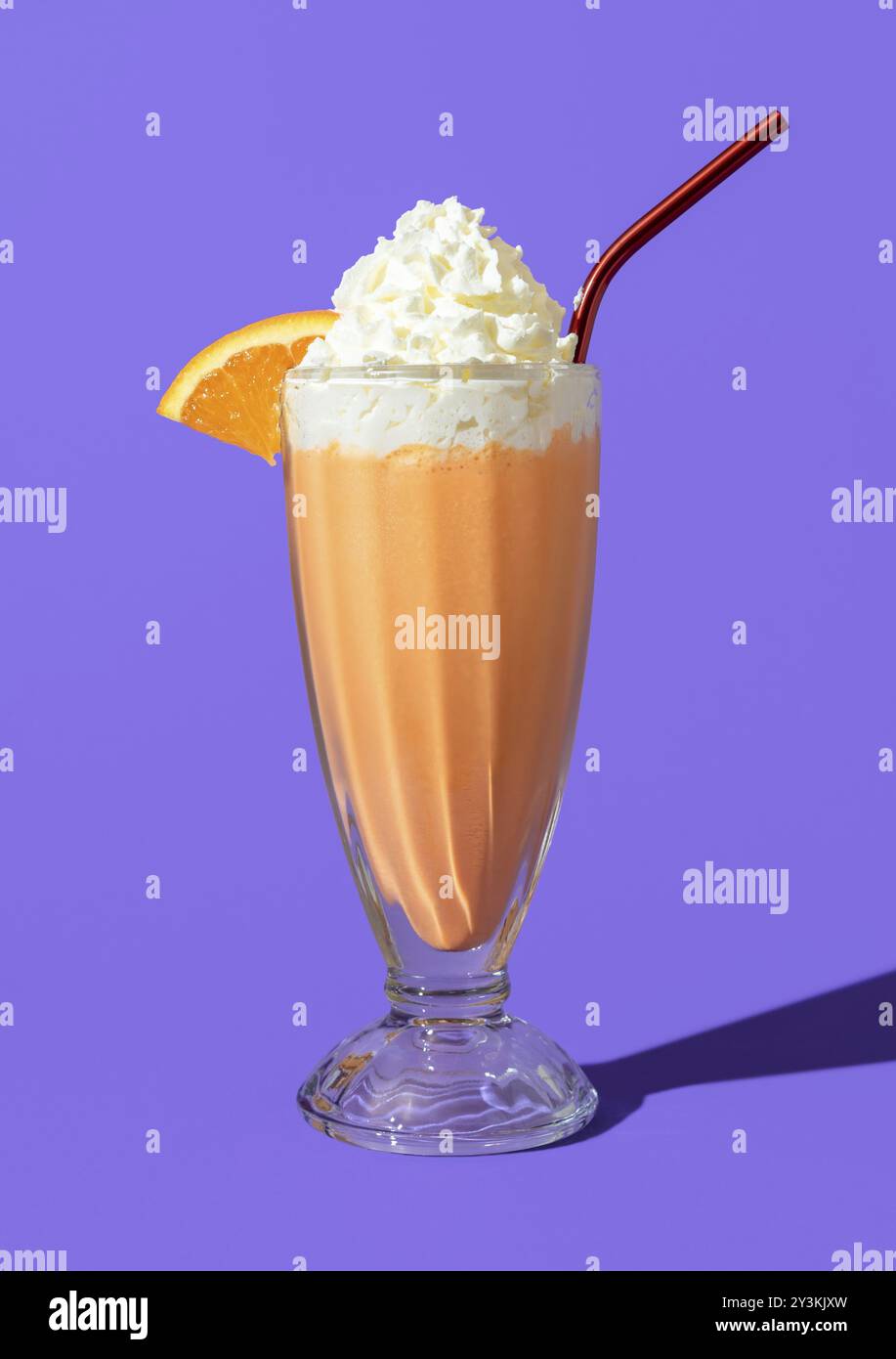 Bicchiere di milkshake fatto in casa con succo d'arancia, gelato alla vaniglia e panna montata. Delizioso milkshake arancione minimalista su sfondo viola Foto Stock