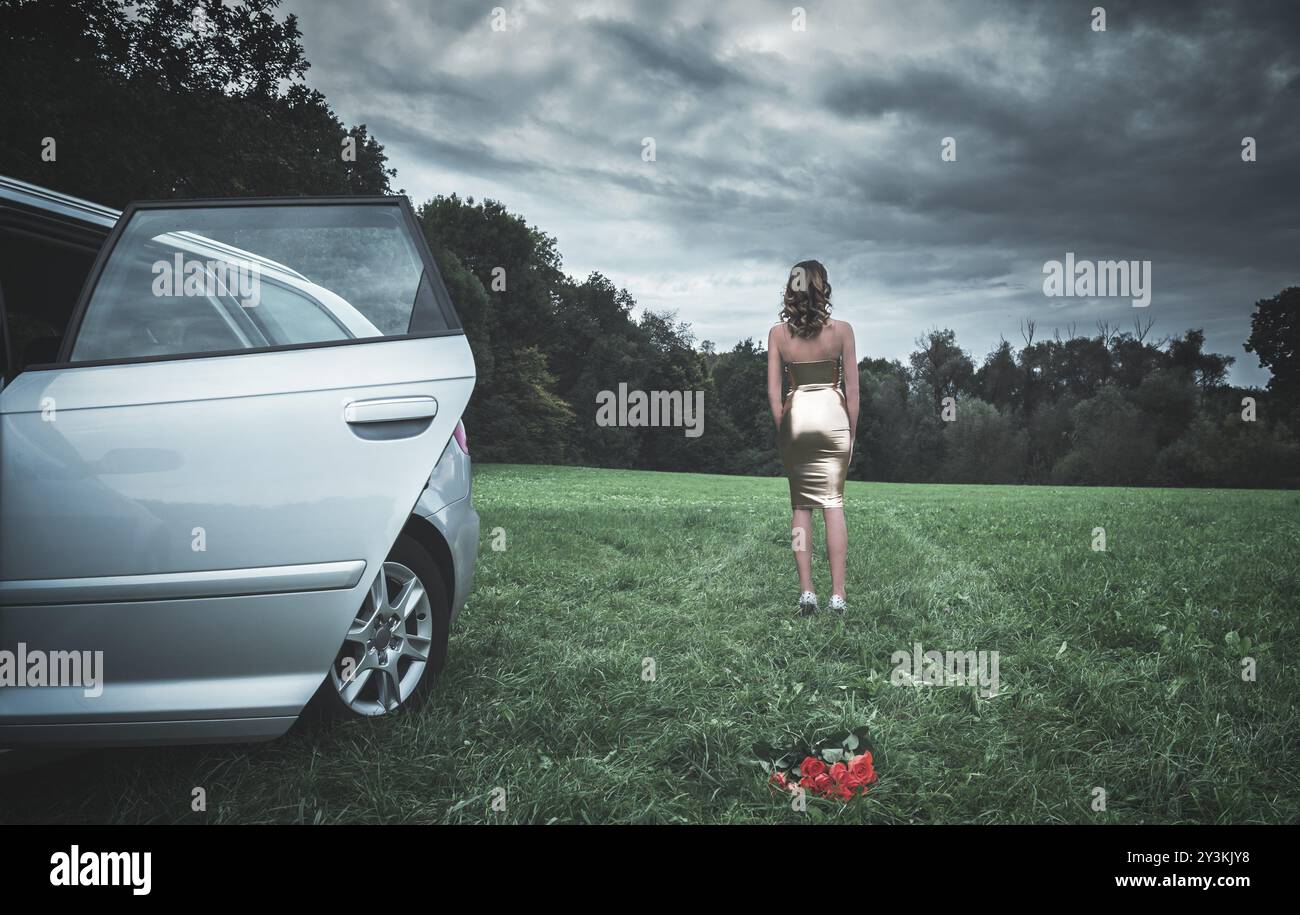 Attraente giovane donna vestita con un abito in lattice dorato, allontanandosi da un'auto e un mazzo di rose sdraiate sull'erba, in una giornata cupa Foto Stock