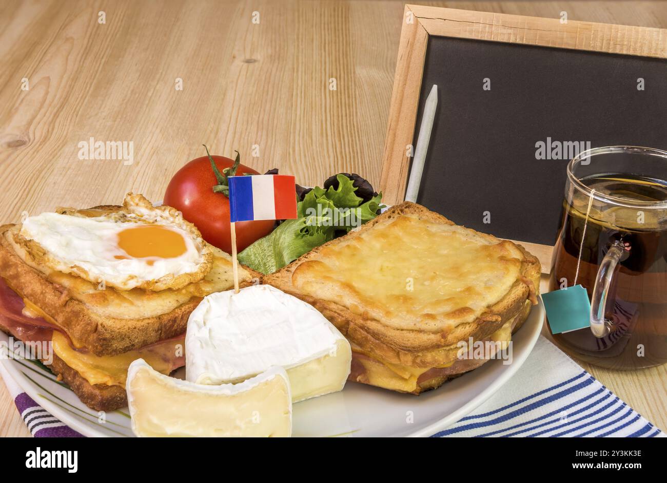 Colazione francese specifica con panini al formaggio fuso, formaggio bianco con bandiera francese, insalata, tazza di tè e lavagna bianca, su un tavolo di legno Foto Stock