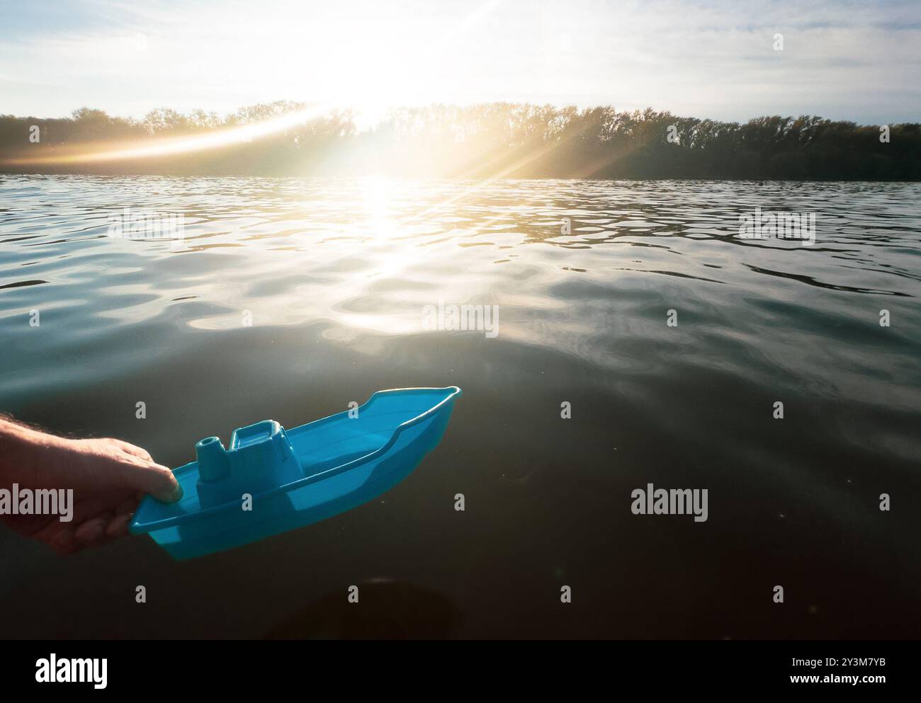 La mano di un uomo lancia una barca giocattolo nel grande fiume. La speranza blu Foto Stock
