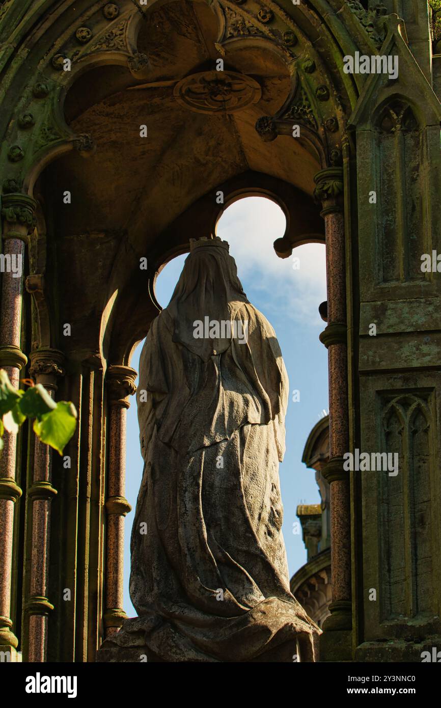 Una statua in pietra di una figura a camicia sorge all'interno di un arco ornato, circondato da intricati dettagli architettonici. Lo sfondo presenta un blu chiaro Foto Stock