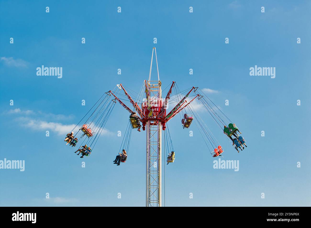 Un colorato giro a dondolo in un parco divertimenti, con più posti a sedere sospesi da una torre centrale. I ciclisti si stanno godendo l'esperienza contro una clea Foto Stock