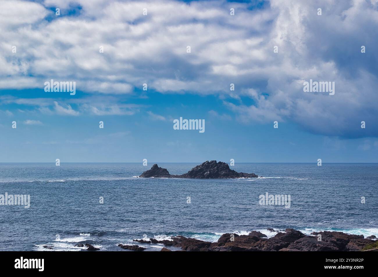 Un tranquillo paesaggio marino caratterizzato da isole rocciose in lontananza sotto un cielo parzialmente nuvoloso. L'oceano è calmo con onde dolci e il primo piano mostra dar Foto Stock