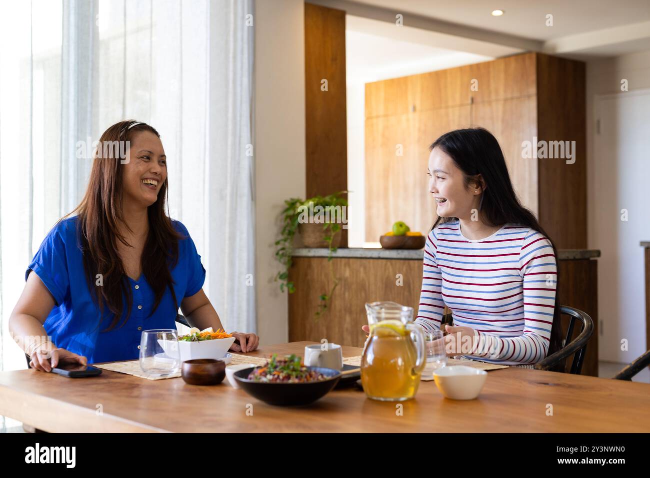 Mamma e figlia asiatiche sorridenti che mangiano insieme al tavolo da pranzo di casa Foto Stock