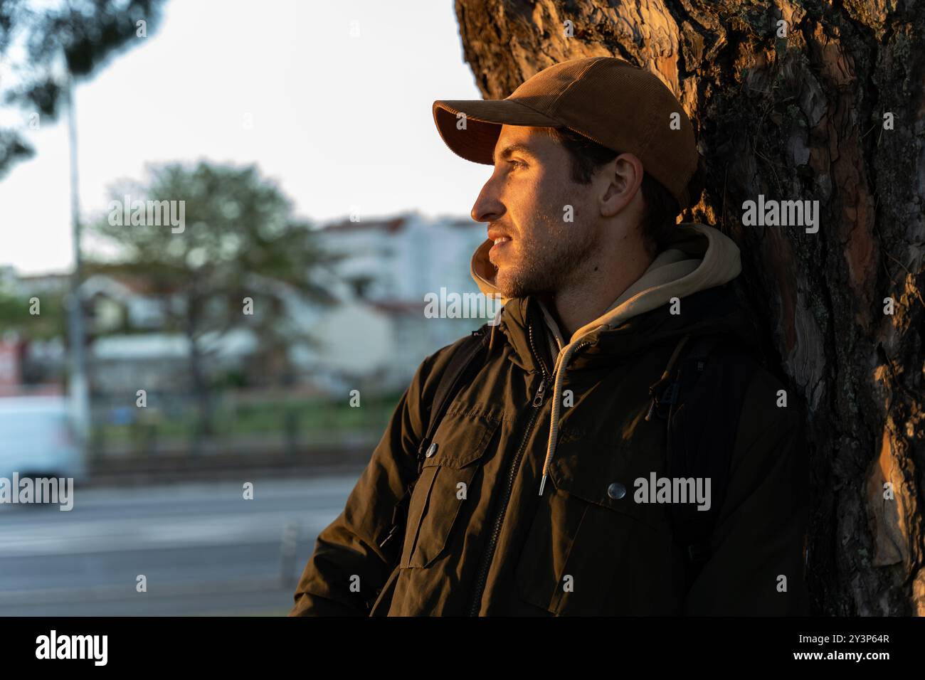 Un uomo appoggiato su un albero in un parco contempla il tramonto e i colori autunnali della città Foto Stock