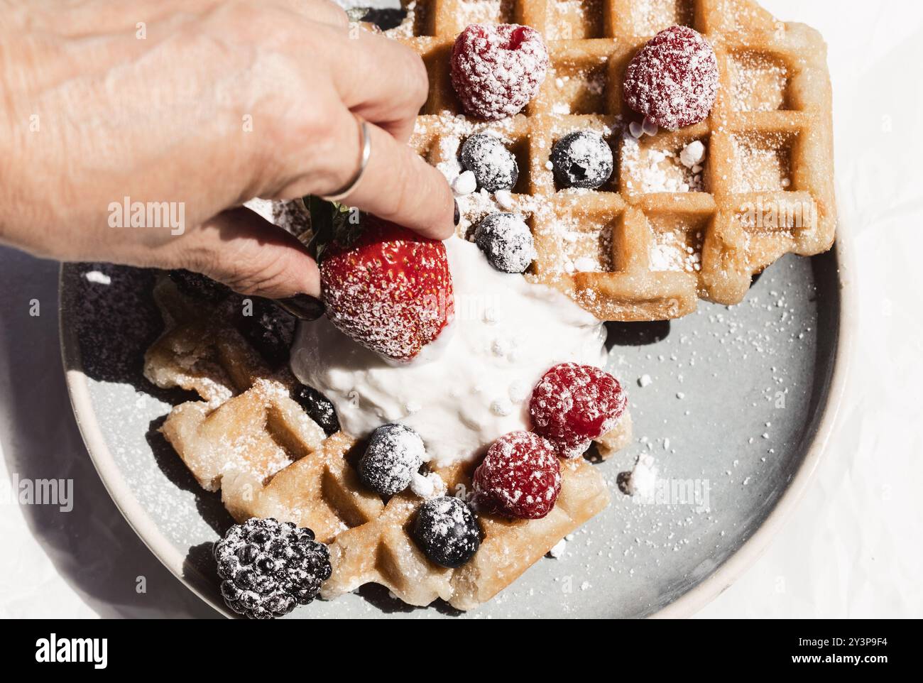 Primo piano con una fragola fresca sopra i waffle dorati guarniti con panna montata, lamponi, more e mirtilli, dus Foto Stock