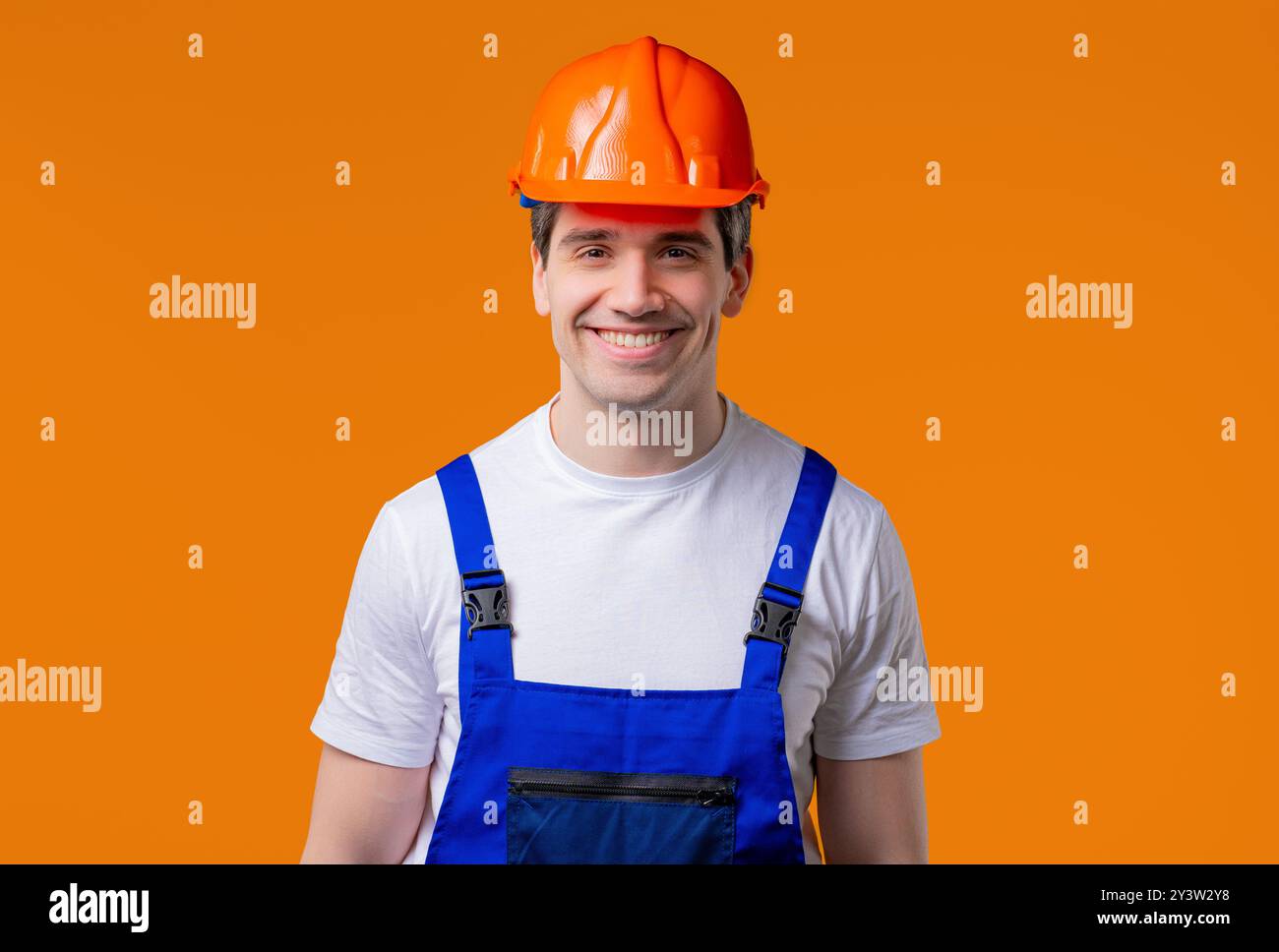 Ritratto sorridente del tuttofare in uno studio arancione. Uomo costruttore positivo, casco Foto Stock