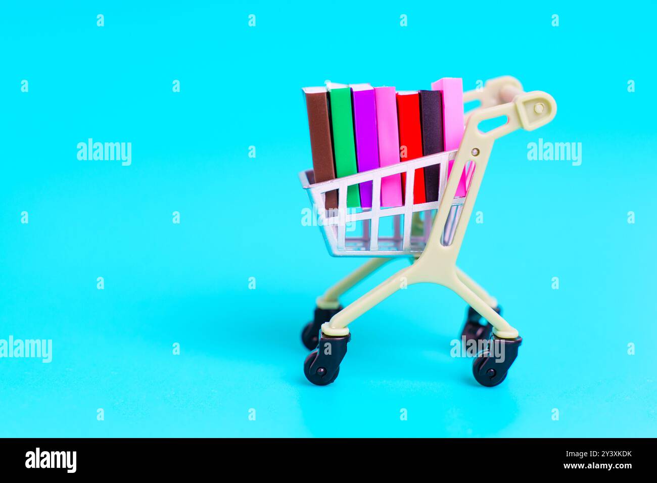 Carrello a spinta in miniatura pieno di libri colorati su sfondo blu. Organizzazione e pianificazione dei materiali di studio. Foto Stock