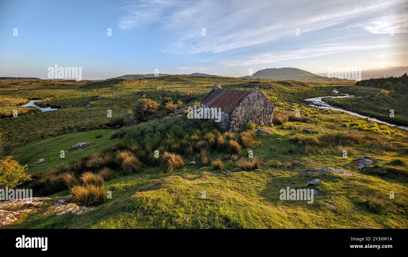 Splendido paesaggio con vecchio cottage con tetto in stagno arrugginito sulla verde collina del Connemara National Park nella contea di Galway, Irlanda, sullo sfondo Foto Stock