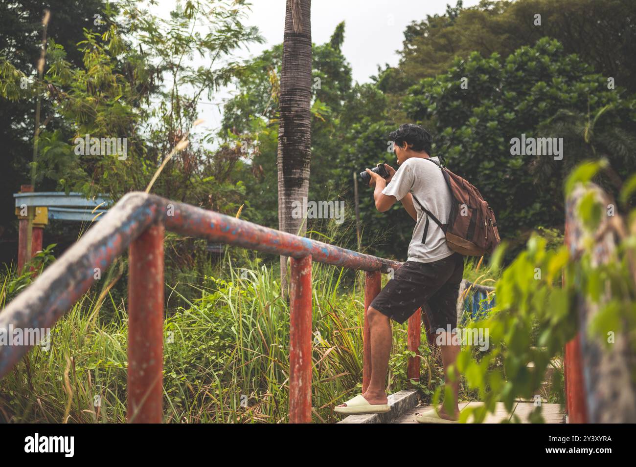 Gli uomini cercano di scattare foto da un parco abbandonato con la macchina fotografica in mano. Zaino in spalla solo in piedi sul bordo del ponte per scattare foto. Foto Stock