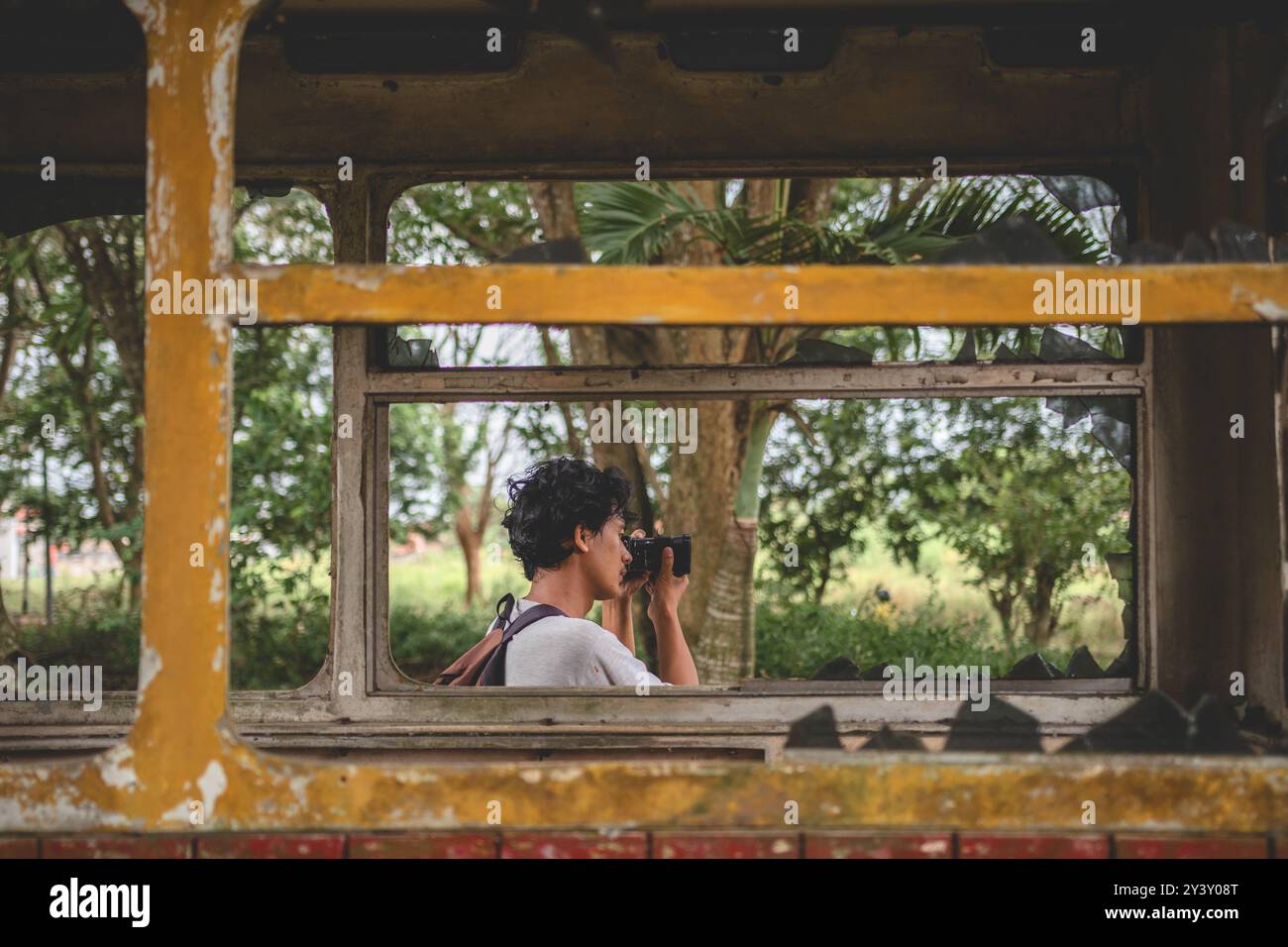 Uomo che punta la fotocamera per scattare una foto. Vista laterale di un giovane uomo con la sua fotocamera che scatta foto. Young male scatta foto da dietro la finestra. Foto Stock